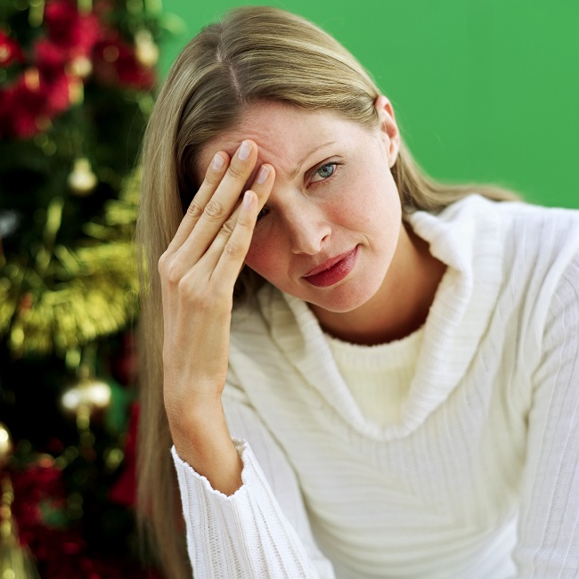 woman sitting beside a Christmas tree with her hand on her forehead