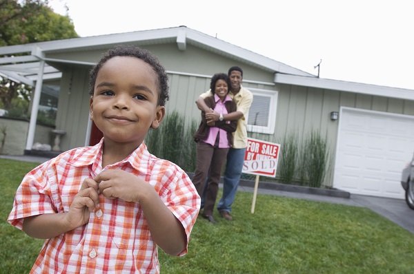 child in front of house with sold sign and parents in backgrond