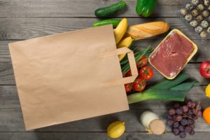 Paper Bag Full Of Different Groceries On Wooden Background Close Up, Top View;